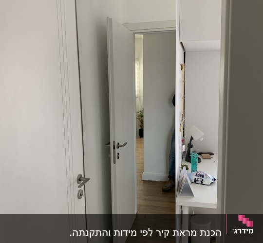 מראה על דלת לבנה בחדר עם רצפת עץ